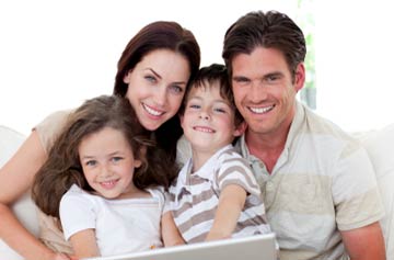 Father, mother and two children setting in front of a laptop computer smiling